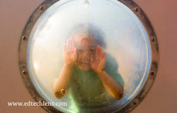 The importance of play: child peeking out of round window on play equipment