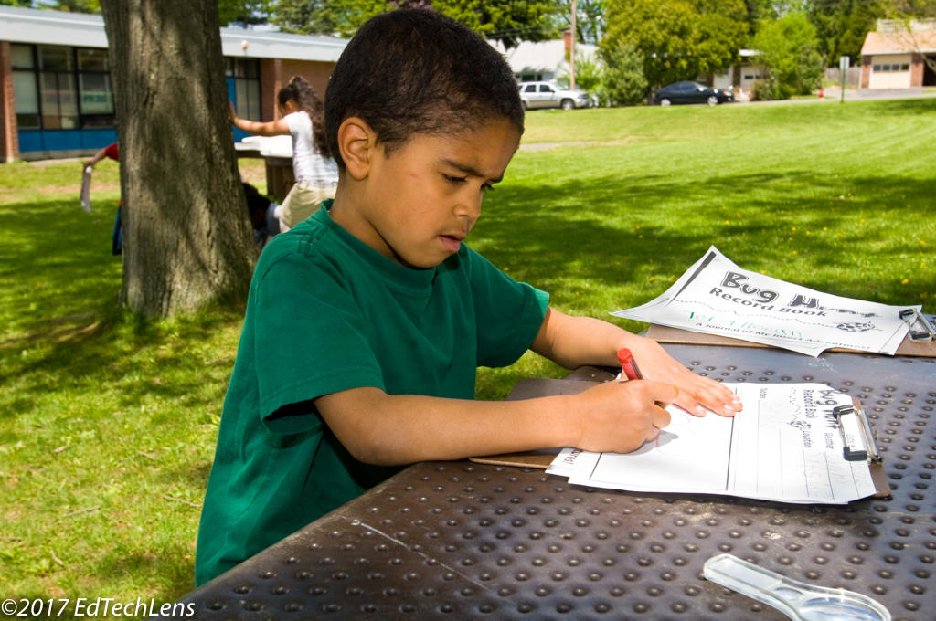 Kindergarten boy writes notes for his science record book after a class bug hunt 