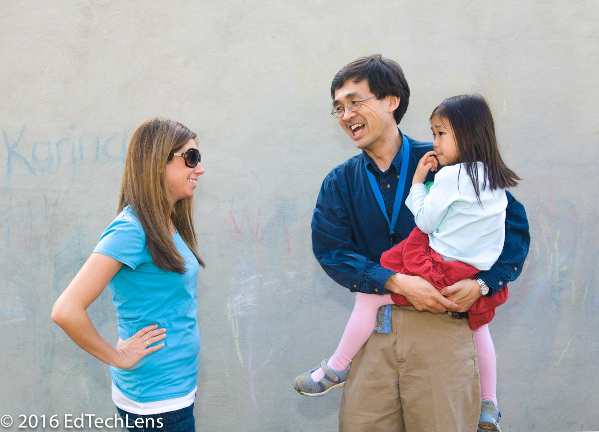 Father holding his daughter and teacher talk at end of school day Father holding his daughter and teacher talk at end of school day