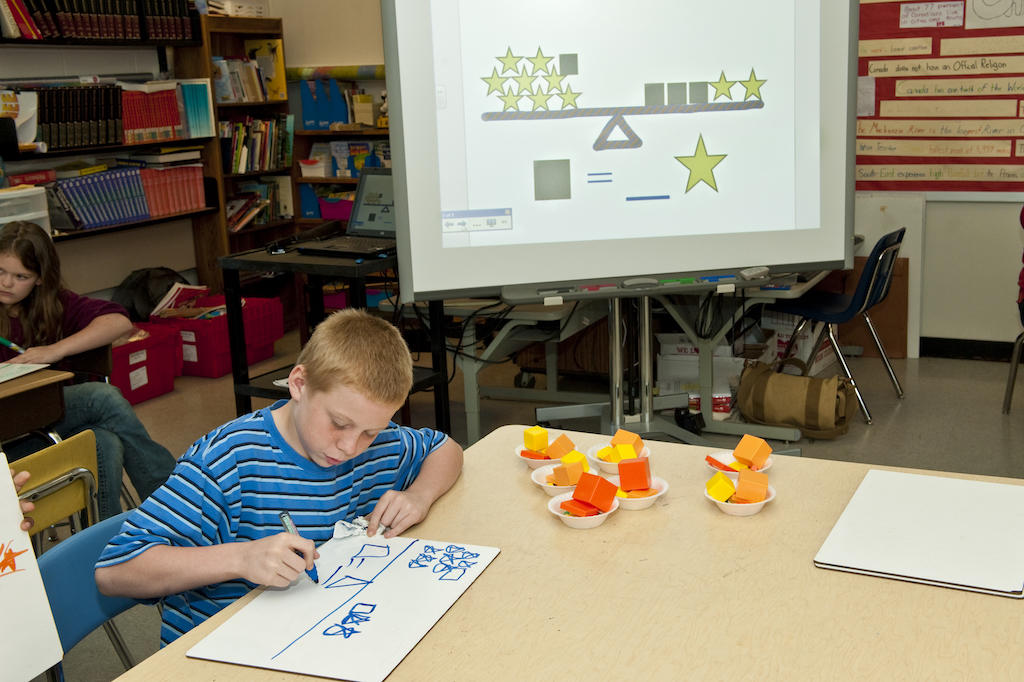 Fifth-grade student uses marker, pencil, physical objects, and digital display while learning about algebraic equations Fifth-grade student uses marker, pencil, physical objects, and digital display while learning about algebraic equations